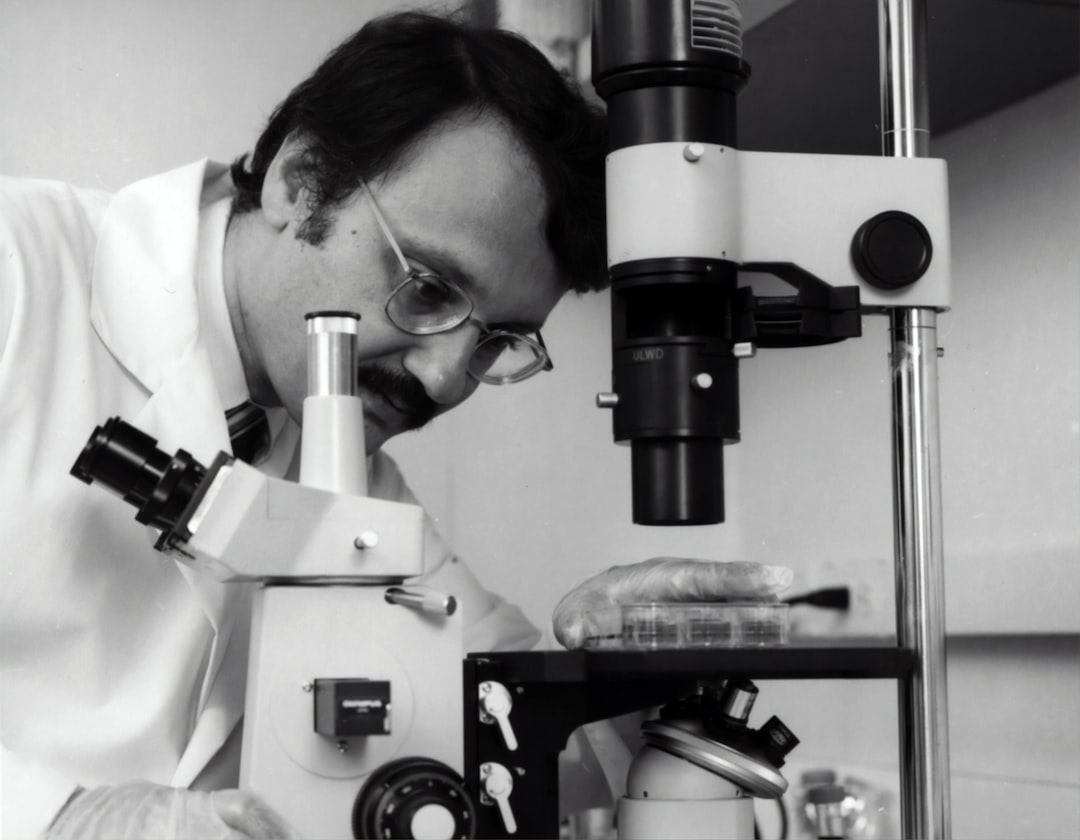 grayscale photography of doctor using microscope