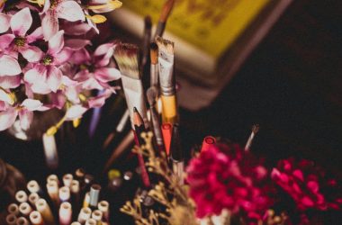 selective focus photography of makeup brush and pencil and pens beside pink and purple flowers
