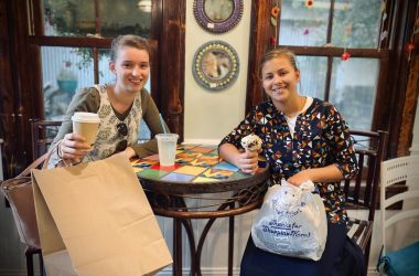 a couple of women sitting at a table with paper bags