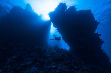 a person scubas through the water near a rock formation