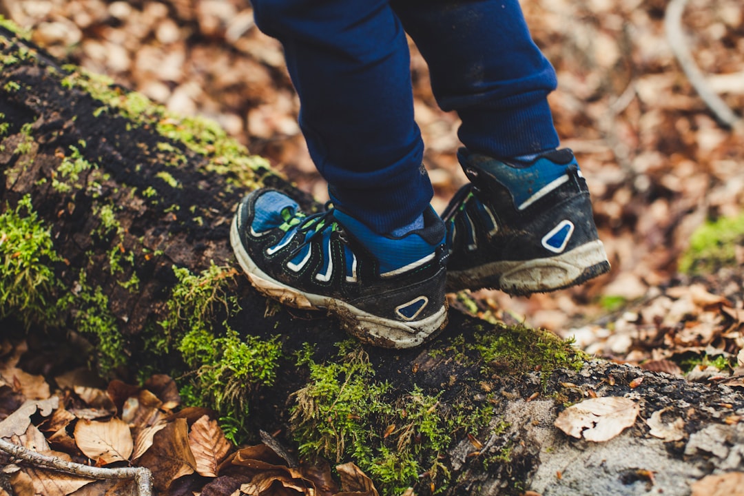 person in blue denim jeans and black and white nike sneakers standing on green moss