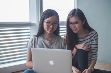 two smiling women starring on silver MacBook inside well-lit room