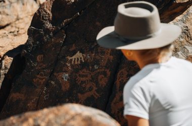 a man wearing a hat standing next to a rock