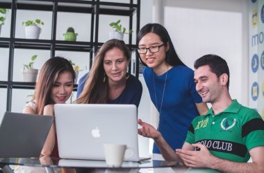 four people watching on white MacBook on top of glass-top table