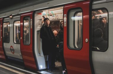 a man standing on a train platform next to a red and silver train