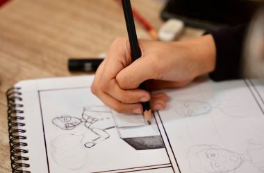 A person holding a pencil and drawing on a book