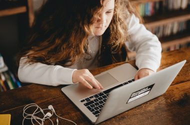 woman in white long sleeve shirt using macbook air on brown wooden table