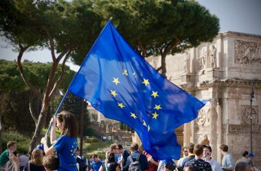 a young girl holding a european flag in front of a crowd of people