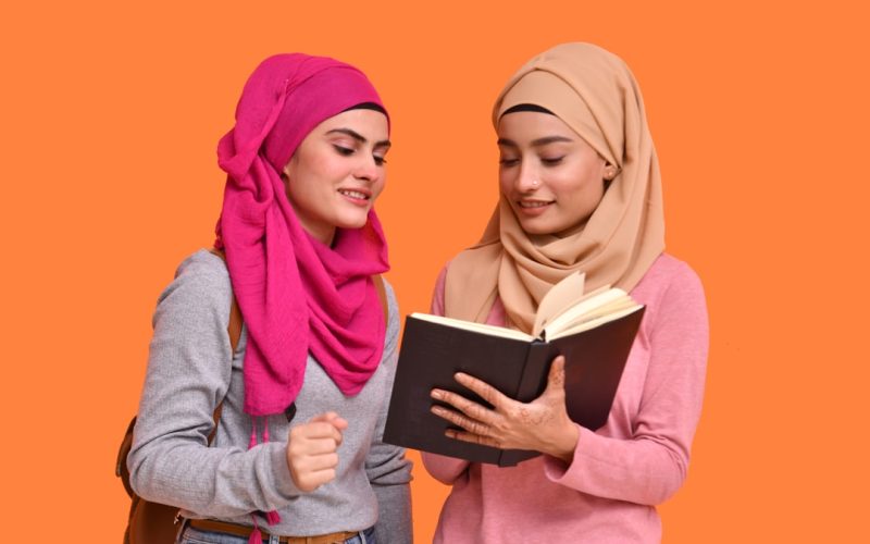 two women in hijabs are reading a book