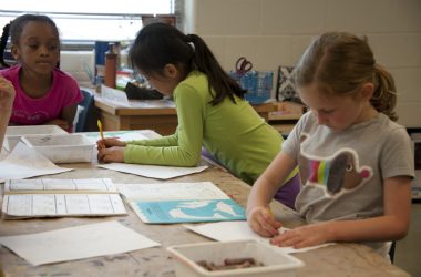 girl in green long sleeve shirt writing on white paper