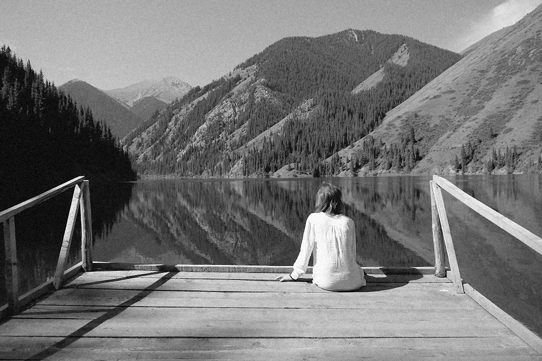 a woman sitting on a dock looking at a mountain lake