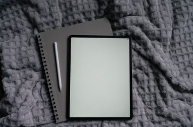 Tablet, notebook, and pen on a gray blanket.