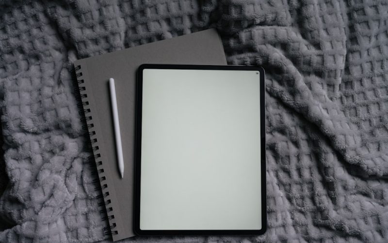 Tablet, notebook, and pen on a gray blanket.