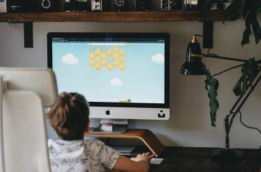 girl in white and blue floral shirt sitting on chair in front of silver imac
