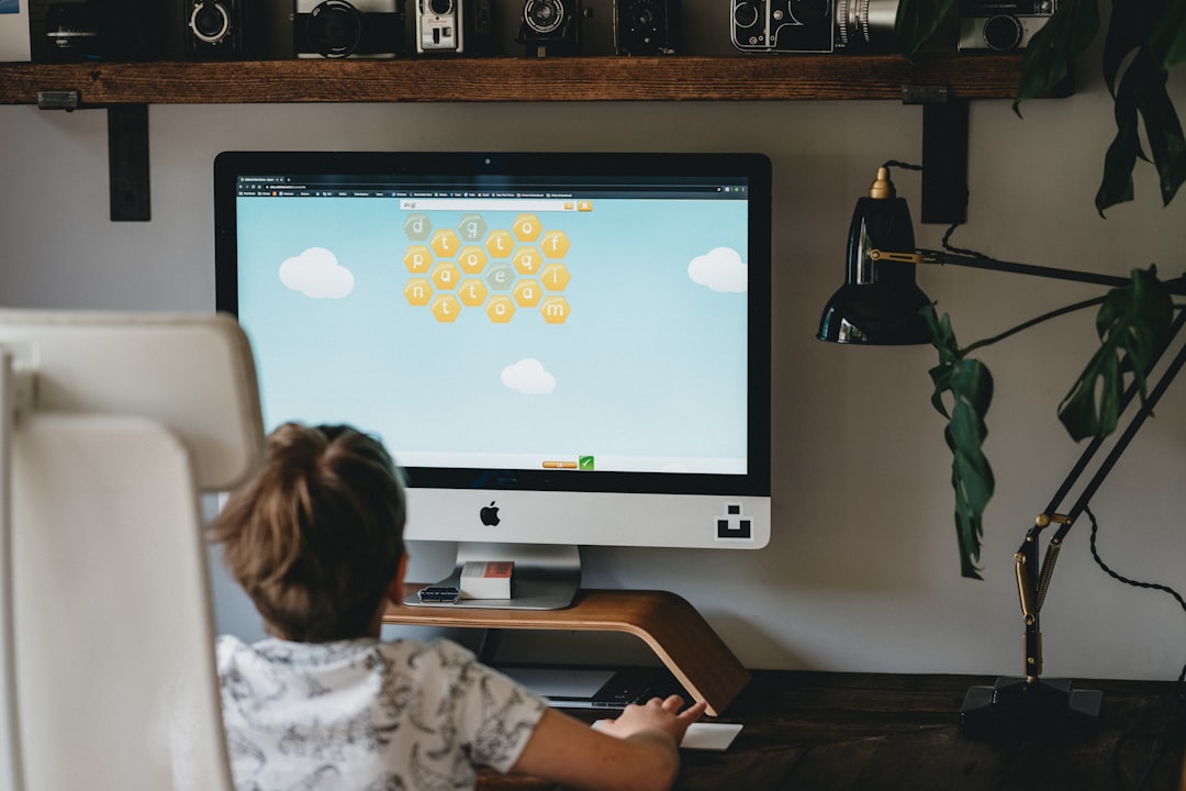 girl in white and blue floral shirt sitting on chair in front of silver imac