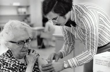 grayscale photography of man holding syringe injecting on woman left arm