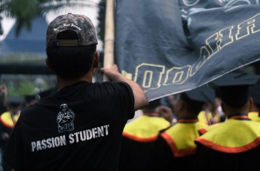 Man in black shirt with "passion student" text holds flag.