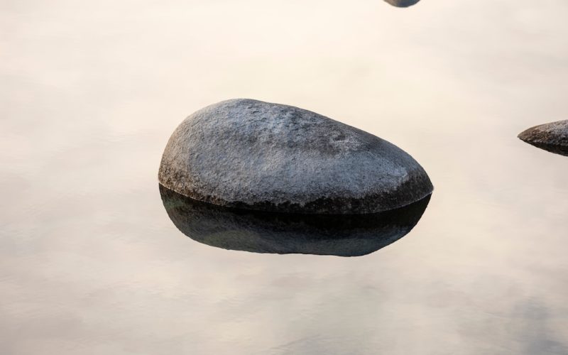 a rock in a body of water with a sky in the background
